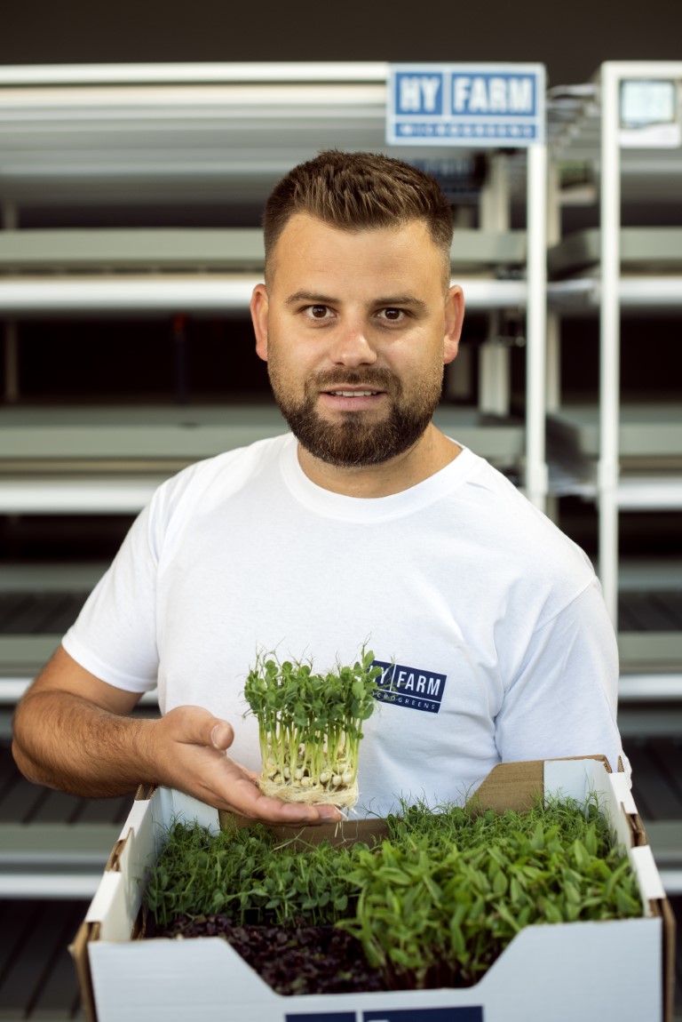 A Hy-Farm specialist holds living microgreens in front of the verified growing system.